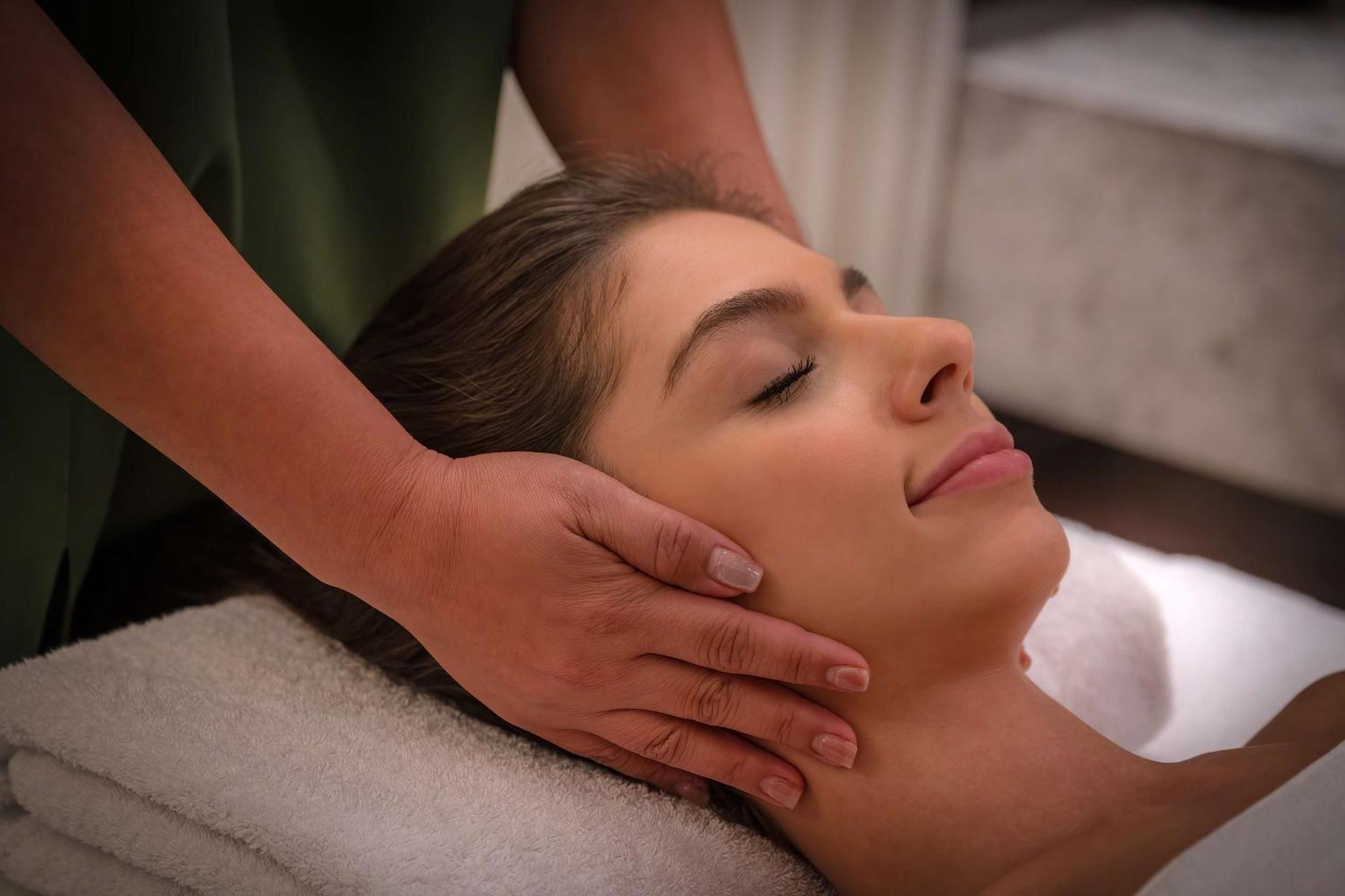 Radisson Blu Hotel, Dubai Deira Creek Exterior photo The image shows a woman lying down with her eyes closed, appearing to be in a state of relaxation. She is receiving a facial massage, with hands gently cradling her head. The setting appears to be a spa or wellness environment, suggesting a focus on 